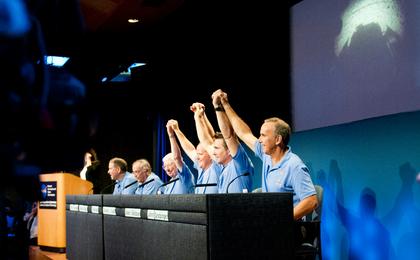 Mars Science Laboratory mission scientists, flight controllers, managers and administrators raise their hands to a cheering crowd at a news conference following the successful landing of NASA's Curiosity rover on Mars.