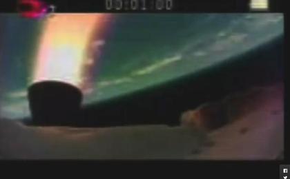 The picture show the LDSD test vehicle and an engine burn in orange/red, with Earth as a blue-green orb in the background.