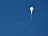 The test vehicle rides on a long, while balloon, against a clear blue sky.