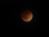 This is an image of the moon during the total lunar eclipse on April 15, 2014. In this image, the moon appears bright orange and is centered on a black sky. Mars is seen a tiny white-red dot on the upper left-hand side of the moon.