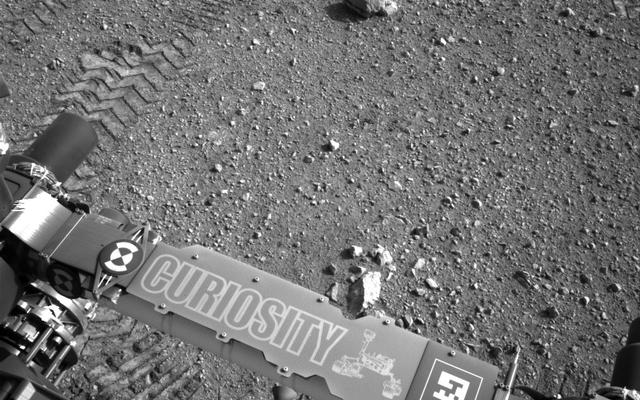 This image shows a close-up of track marks from the first test drive of NASA's Curiosity rover. The rover's arm is visible in the foreground.