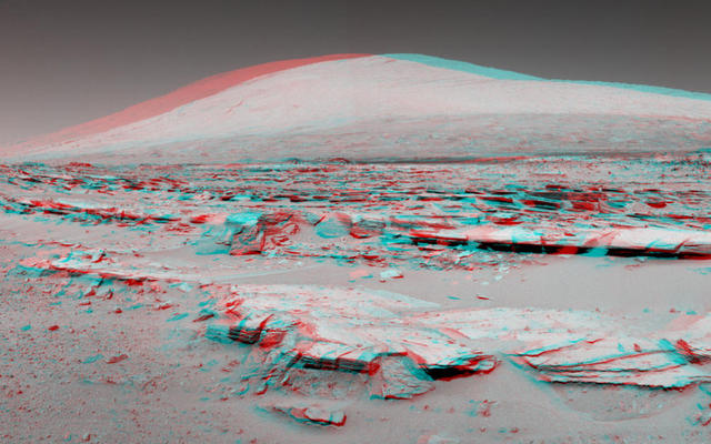 A stereo landscape scene from NASA's Curiosity Mars rover shows rock rows at "Junda" forming striations in the foreground, with Mount Sharp on the horizon. The image appears three dimensional when viewed through red-blue glasses with the red lens on the left.