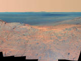 This May 14, 2014, scene from the Pancam on NASA's Mars Exploration Rover Opportunity catches "Pillinger Point," on the western rim of Endeavour Crater, in the foreground and the crater's eastern rim on the horizon. The scene's false color makes differences in surface materials more easily visible.