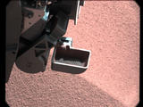 In this image, the scoop on NASA's Curiosity rover shows the larger soil particles that were too big to filter through a sample-processing sieve that is porous only to particles less than 0.006 inches (150 microns) across.