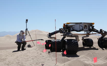 sand dune, mars rover, wheel, Dumont, Scarecrow, test - This image shows the scarecrow test rover going over a dunes obstacle course, while an engineer hunches down to see the wheels as it drives.