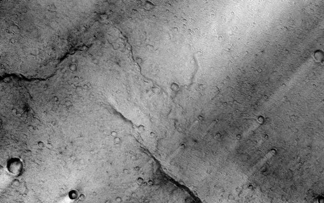 This image is near the southern edge of a low, broad volcanic feature called Syrtis Major. A close look at this image reveals a wrinkly texture that indicates a very rough surface that is associated with the lava flows that cover this region. On a larger scale, there are numerous bright streaks that trail topographic features such as craters. These bright streaks are in the wind shadows of the craters where dust that settles onto the surface is not as easily scoured away. It is important to note that these streaks are only bright in a relative sense to the surrounding image. Syrtis Major is one of the darkest regions on Mars and it is as dark as fresh basalt flows or dunes are on Earth.