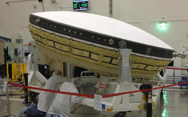NASA workers at JPL wearing clean room, white "bunny suits," prepare a large saucer-shaped test vehicle that will be used to land larger payloads on Mars.