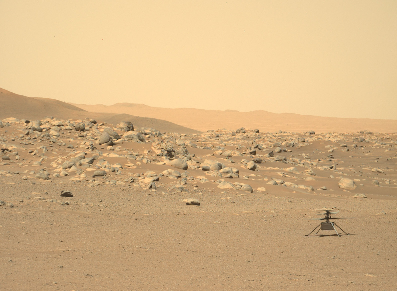 NASA's Mars Perseverance rover acquired this image using its Left Mastcam-Z camera. It displays the helicopter on the ground sitting on the sandy surface of Mars with rocks and hills in the background.