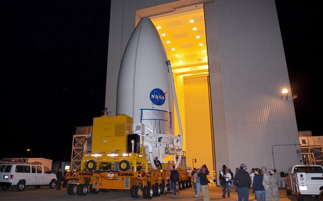 Standing atop a payload transporter, the Atlas V rocket payload fairing containing NASA's Mars Science Laboratory (MSL) spacecraft rolls out of the Payload Hazardous Servicing Facility at Kennedy Space Center in Florida, beginning the move to Space Launch Complex 41.
