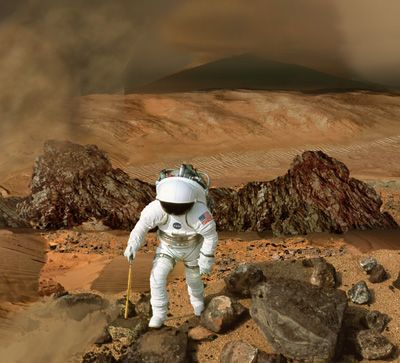 This image shows a backward-looking view of an astronaut in a white spacesuit hiking over reddish sand and rocks on Mars. A gray plume of smoke rises from a fumarole behind the astronaut.