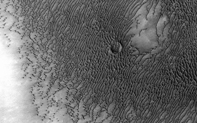 A vast dune field lies near the northern polar cap of Mars. Seen here in summer, the dunes have partially buried an impact crater about 1,000 meters (3,300 feet) wide.