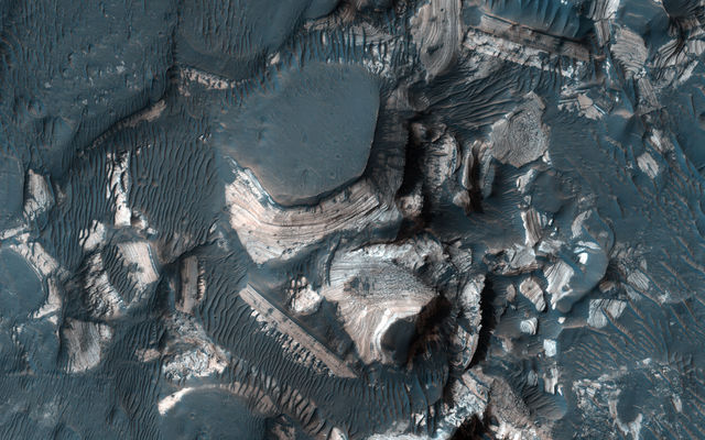 This image shows blocks of bright, layered rock embedded in darker material that are thought to have been deposited by a giant flood that occurred when Uzboi Valles breached the rim of Holden Crater.