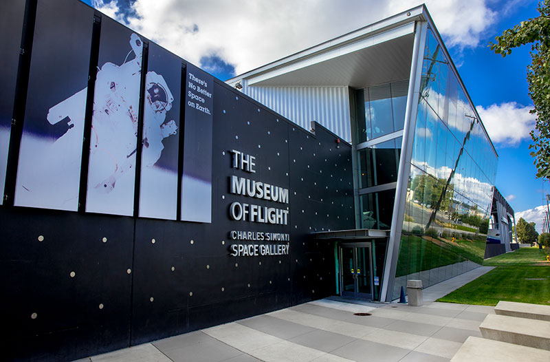 An image of the front entrance of The Museum of Flight, showing a picture of an astronaut in space and a modern glass wall.