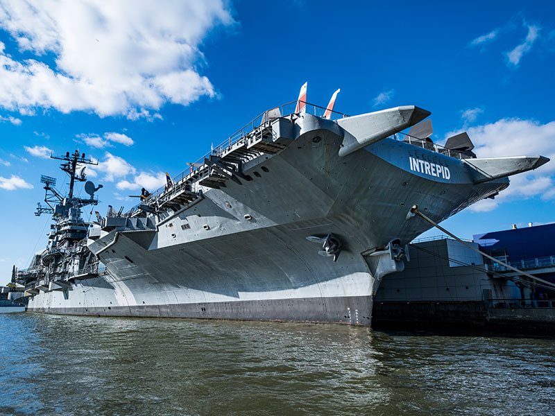 An image of the Intrepid museum, which is located on the USS Intrepid, a large ship docked on a pier in New York, NY.