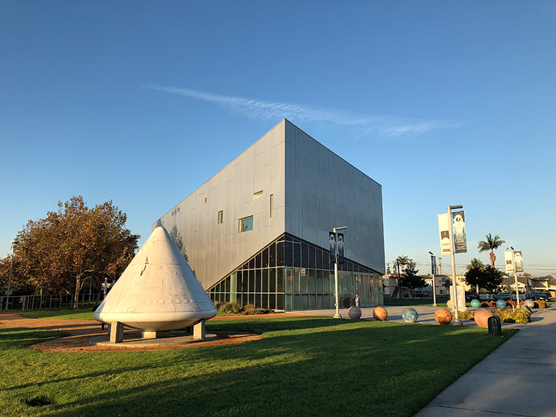 An image of the museum with a modern metal and glass entrance and a NASA capsule in front of it.