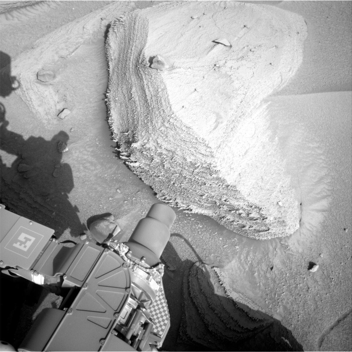 This image shows part of the Curiosity rover's instruments and shadow above the Mars surface, ahead of a rock formation.