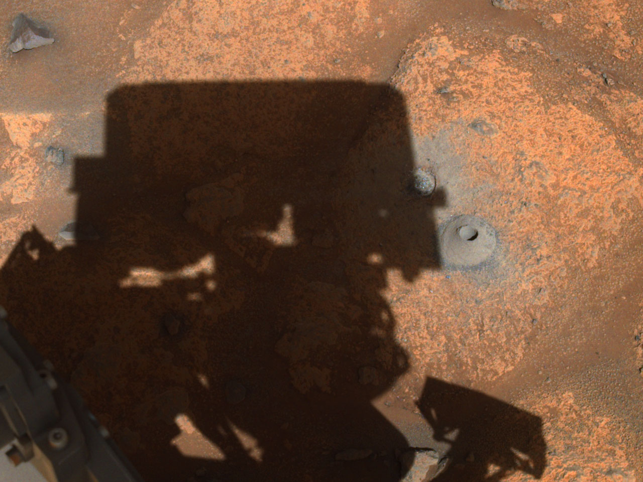 The drill hole from Perseverance’s first sample-collection attempt can be seen, along with the shadow of the rover, in this image taken by one of the rover’s navigation cameras. 