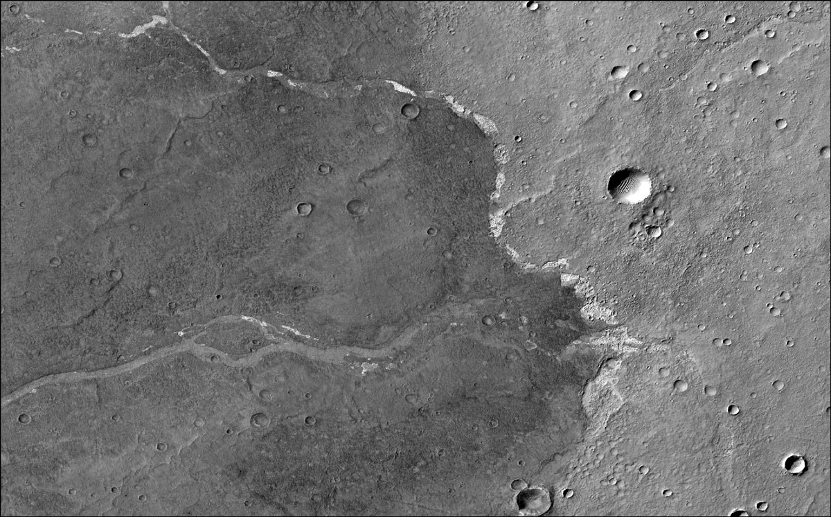 NASA’s Mars Reconnaissance Orbiter used its Context Camera to capture this image of Bosporos Planum, a location on Mars. The white specks are salt deposits found within a dry channel. The largest impact crater in the scene is nearly 1 mile (1.5 kilometers) across.