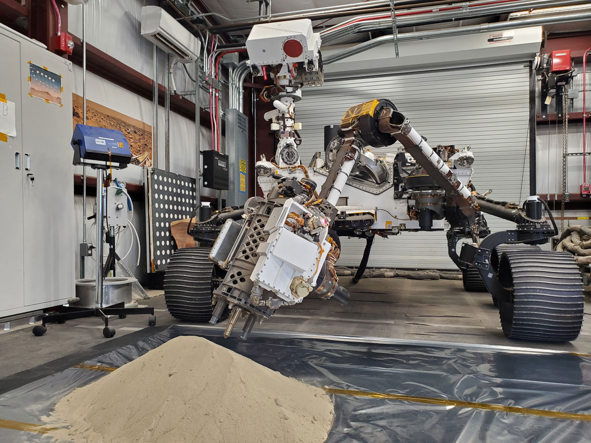 Optimism, a full-scale replica of NASA’s Perseverance Mars rover, tests a model of Perseverance’s regolith bit in a pile of simulated regolith – broken rock and dust – at JPL. 