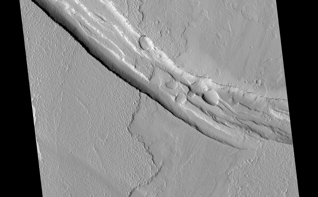 This image shows a graben (a trough formed when the ground drops between two parallel faults) and a lava flow in the Tharsis volcanic province of Mars. North is up.