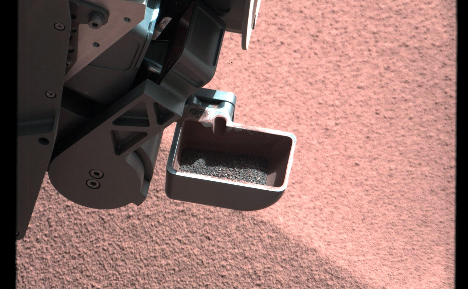 In this image, the scoop on NASA's Curiosity rover shows the larger soil particles that were too big to filter through a sample-processing sieve that is porous only to particles less than 0.006 inches (150 microns) across.