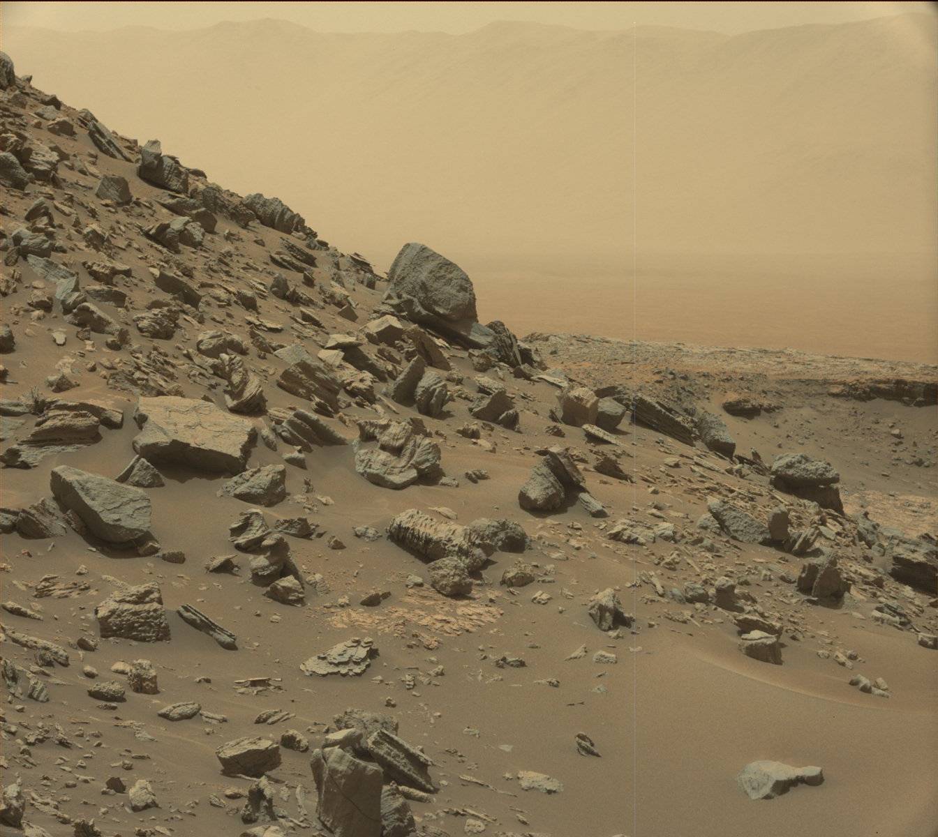 The rim of Gale Crater is visible in the distance, through the dusty haze, in this Curiosity view of a sloping hillside on Mount Sharp