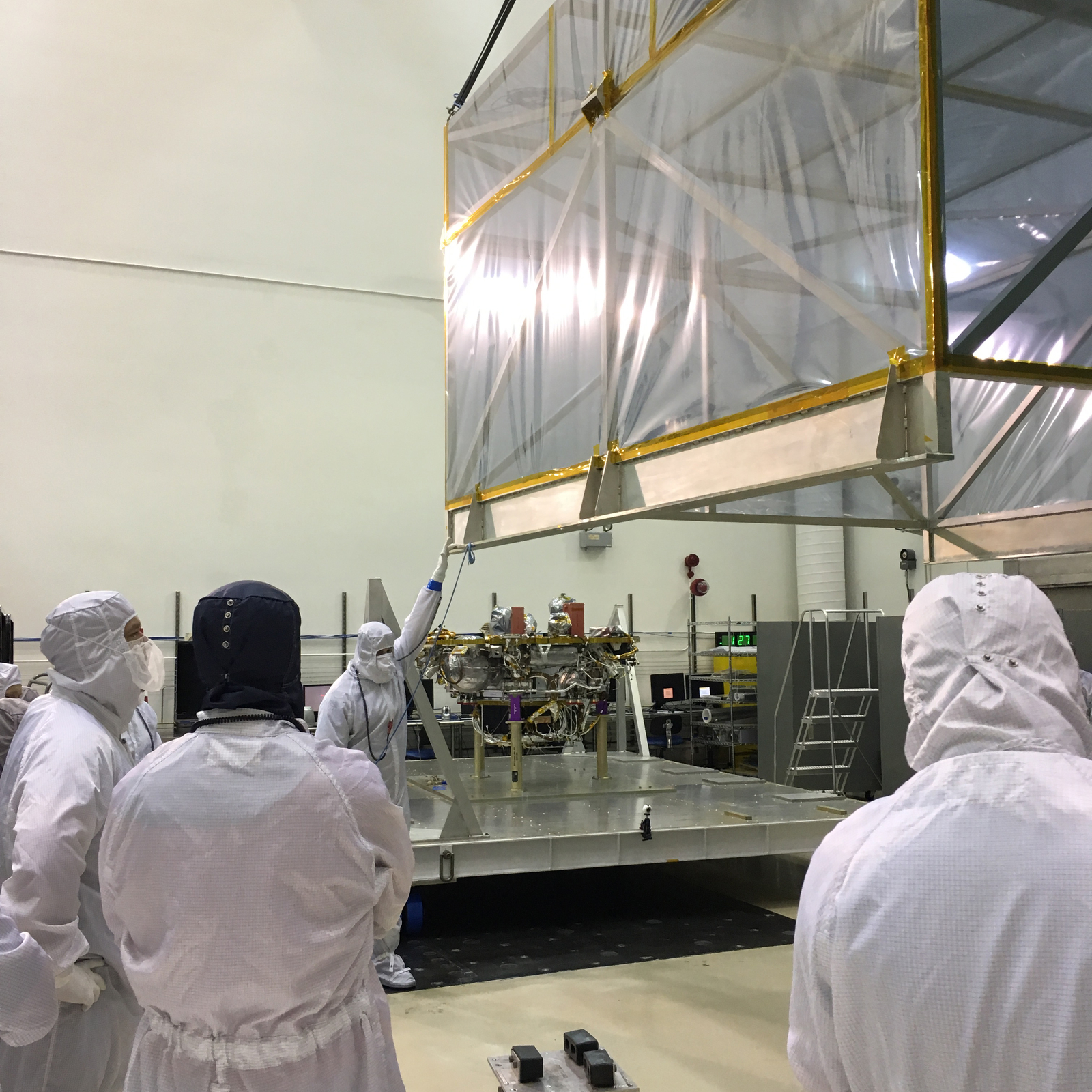 In a Lockheed Martin clean room facility near Denver in June 2017, members of the InSight mission's assembly, test and launch operations team remove the inner layer of protective housing that covered NASA's InSight spacecraft while the spacecraft was in storage after a launch postponement.