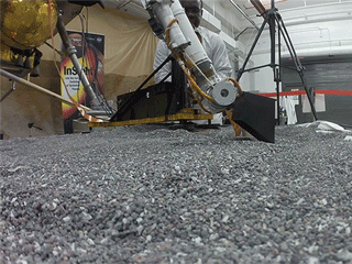 Animated view of a replica of InSight scraping soil with a scoop 